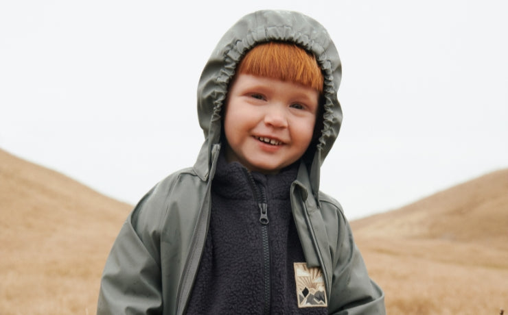 Child wearing a gray hooded jacket with a logo on a desert background
