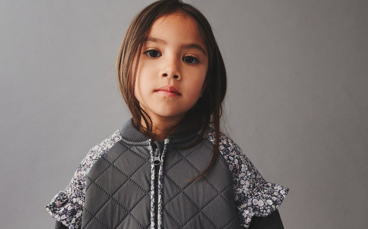Young girl wearing a gray quilted jacket with floral trim against a gray background